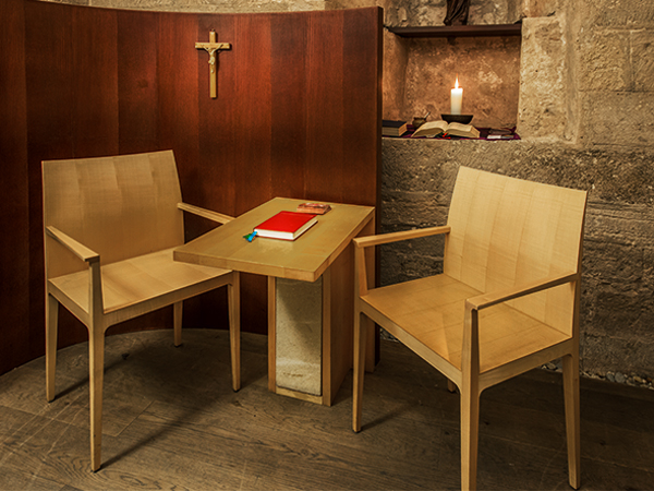Confesionario con sillas, mesa, sagrada cruz, velas y libro rojo